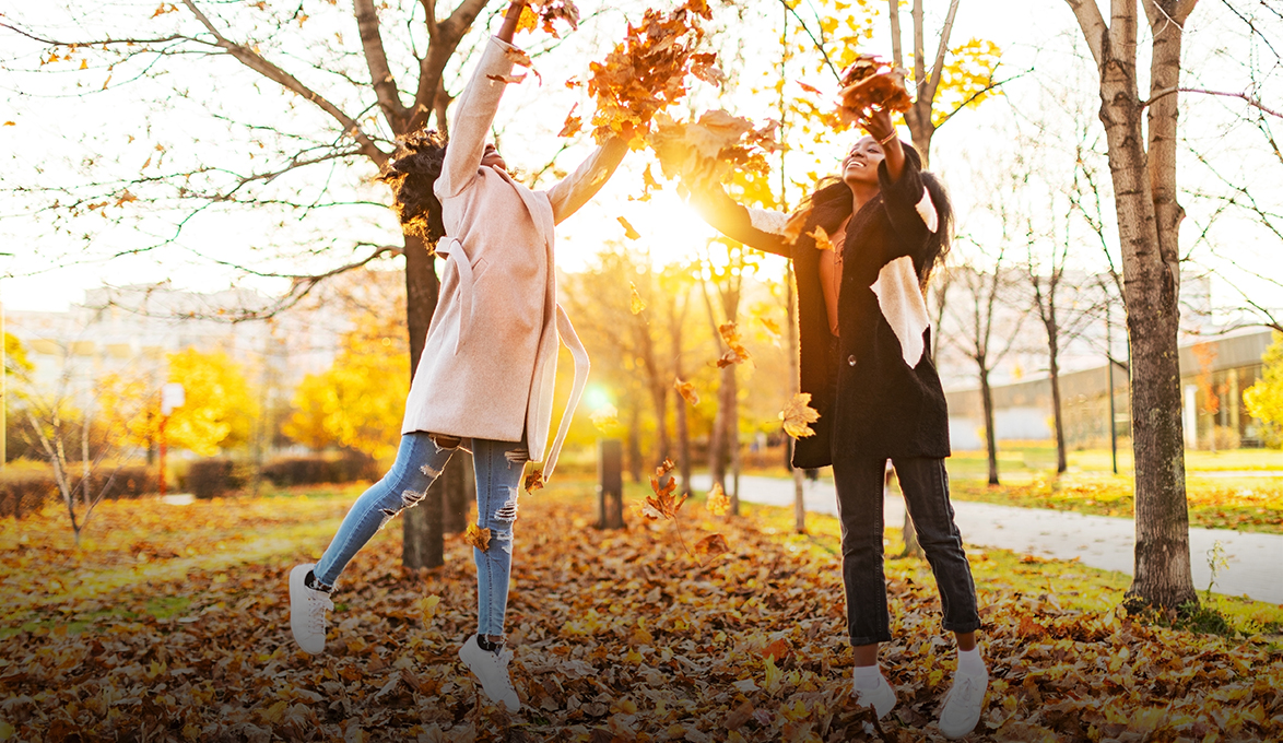 Two young women scattering fall leaves